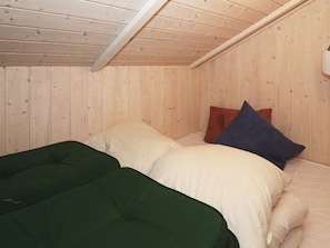 A room with wooden walls and a sloped ceiling. There are two beds with pillows and a green blanket. - 4 Star Holiday Home in Hadsund (Hadsund)
