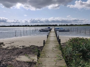 A wooden pier leading to boats on calm water, surrounded by vegetation and a cloudy sky. - 4 Star Holiday Home in Hadsund (Hadsund)