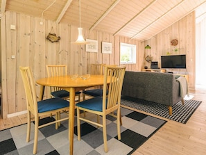 A wooden interior with a round dining table, blue cushioned chairs, a sofa, a television, and a patterned rug. - 4 Star Holiday Home in Hadsund (Hadsund)