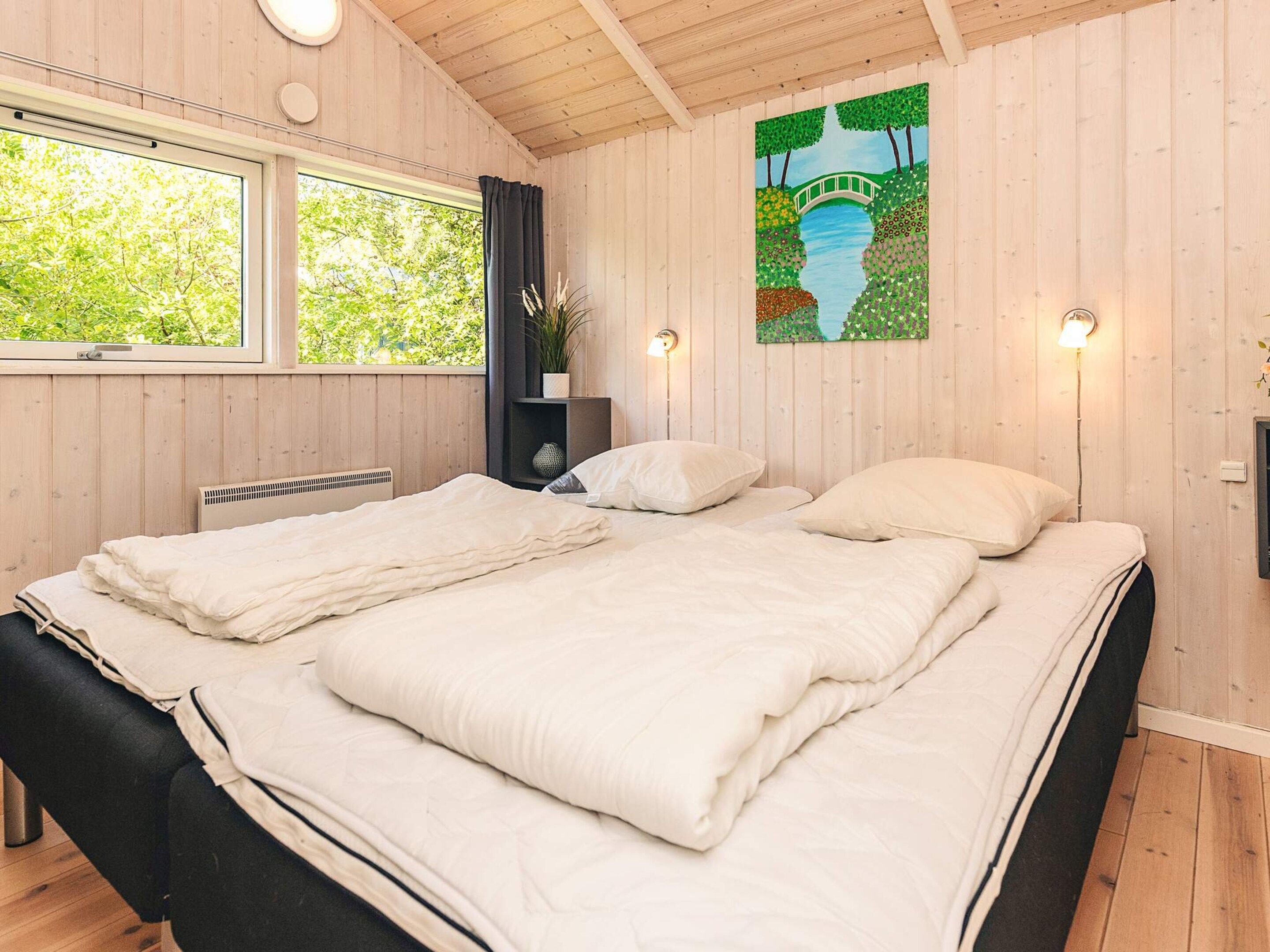 Un lit double avec une literie blanche, dans une pièce aux murs en bois et dotée d’une grande fenêtre.