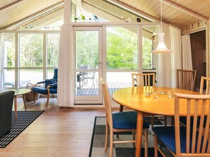 A wooden-floored room with a large table and chairs, a wicker chair, and a view through a glass door to an outdoor deck.