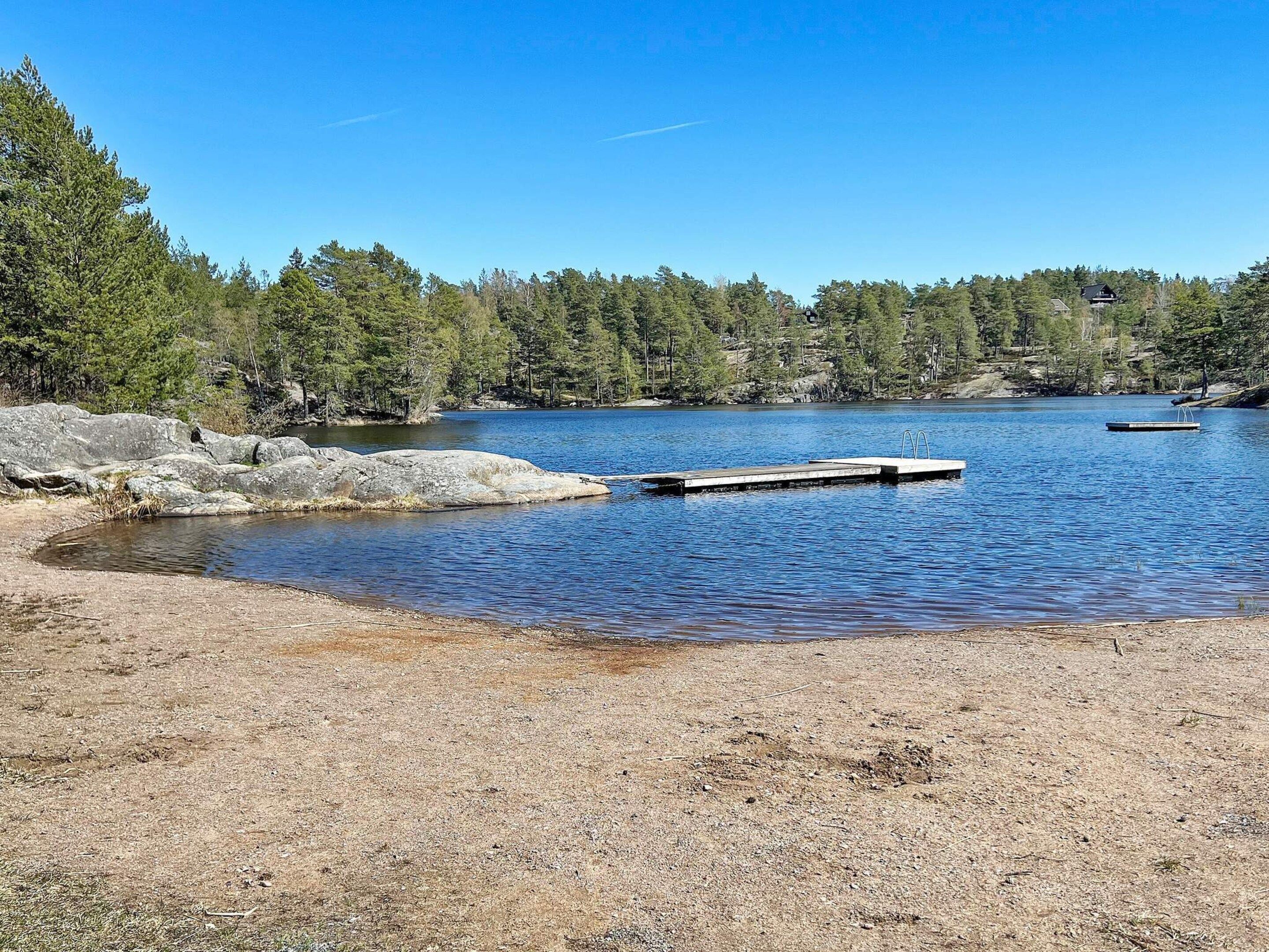 A clear lake with a dock, surrounded by trees and rocky terrain.