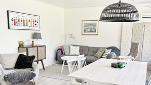 A living room with a white sofa, a dining table, and a lamp. - 6 Person Holiday Home in Djurhamn (Fågelbrolandet)
