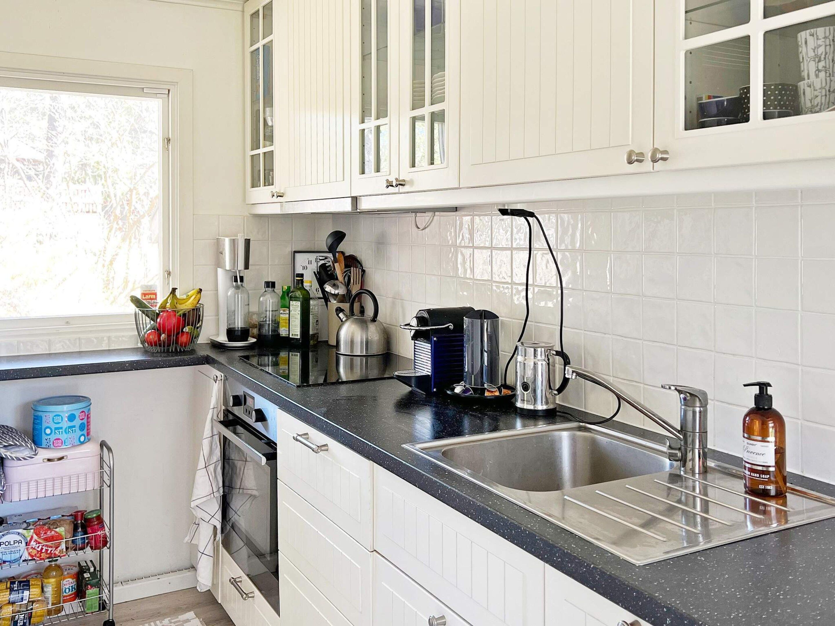 A kitchen with white cabinets, a black countertop, a stainless steel sink, a coffee maker, and a bottle of hand soap.