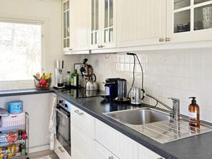 Een keuken met witte kasten, een zwart aanrecht, een roestvrijstalen spoelbak, een koffiezetapparaat en een fles handzeep.