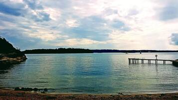 A calm lake with a wooden pier extending into the water, surrounded by a rocky shoreline and distant trees.