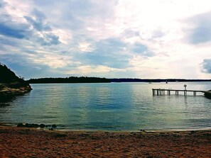 A calm lake with a wooden pier extending into the water, surrounded by a rocky shoreline and distant trees. - 6 Person Holiday Home in Djurhamn (Fågelbrolandet)