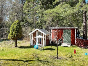 Eine kleine Holzhütte mit Veranda und Schuppen in einer grünen Umgebung, umgeben von Bäumen.