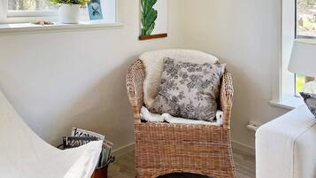 A wicker chair with a floral pillow, a potted plant, and a framed botanical print on a wall.