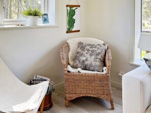 Een rieten stoel met een bloemenkussen, een plant in pot en een lijst met een botanische tekening aan de muur.