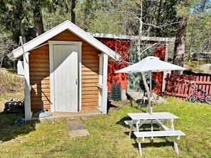 A wooden shed with a door, a picnic table, and a grill in a backyard. - 6 Person Holiday Home in Djurhamn (Fågelbrolandet)