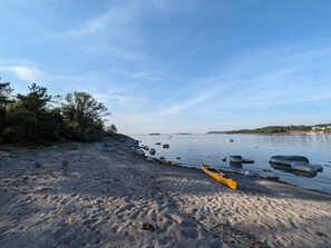 Ein Strand mit Kajaks, ruhigem Wasser und weiter Küste im Hintergrund.