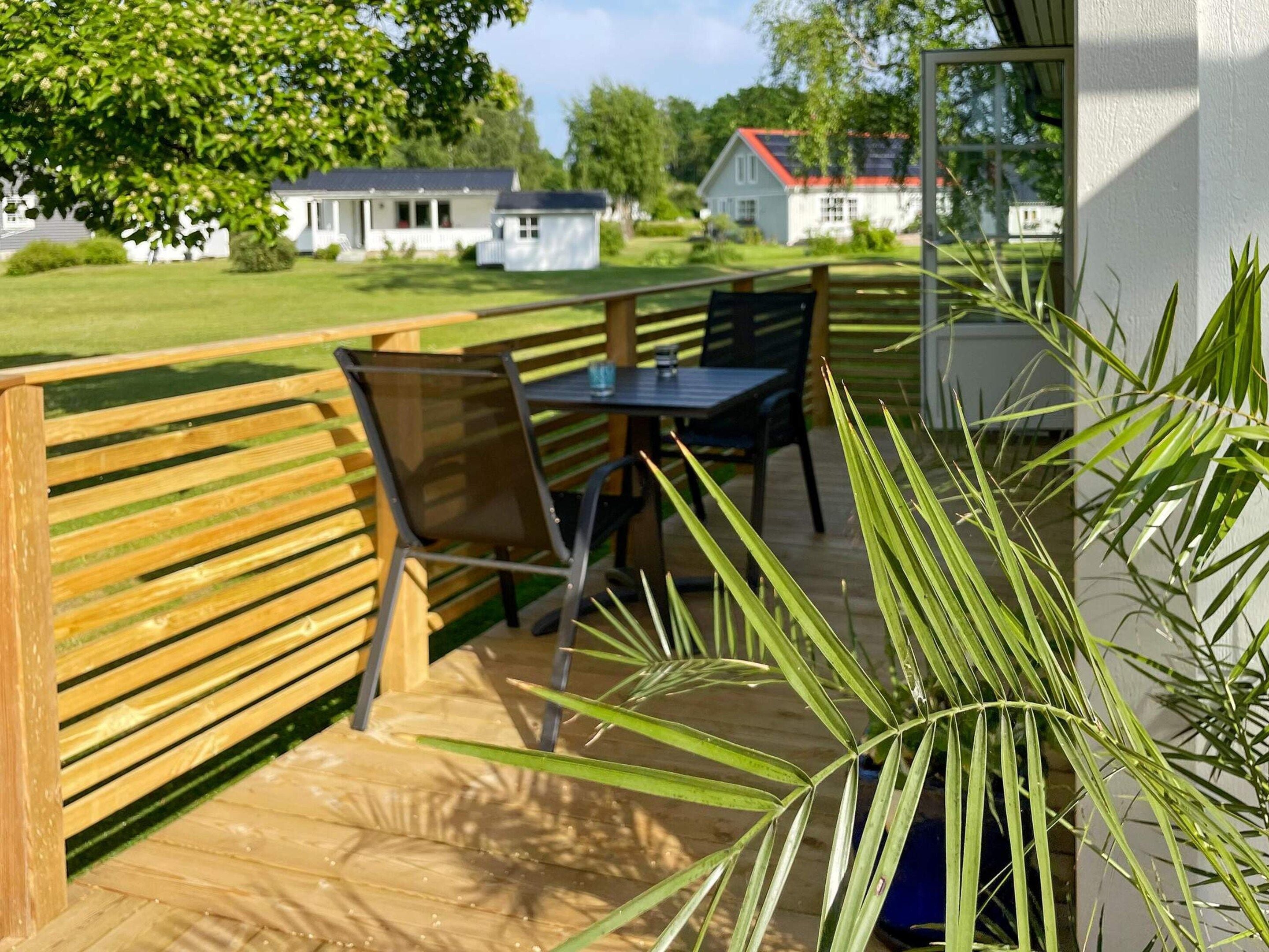 An outdoor seating area with a wooden bench and a table, surrounded by greenery.