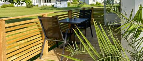 An outdoor seating area with a wooden bench and a table, surrounded by greenery.