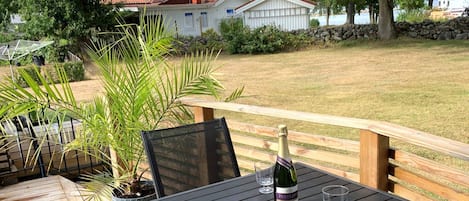 A wooden deck with a table, a bottle of wine, and two glasses.