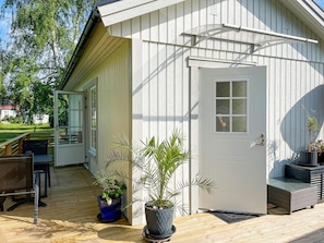 A white building with a door, a window, and a porch with a table and chairs.