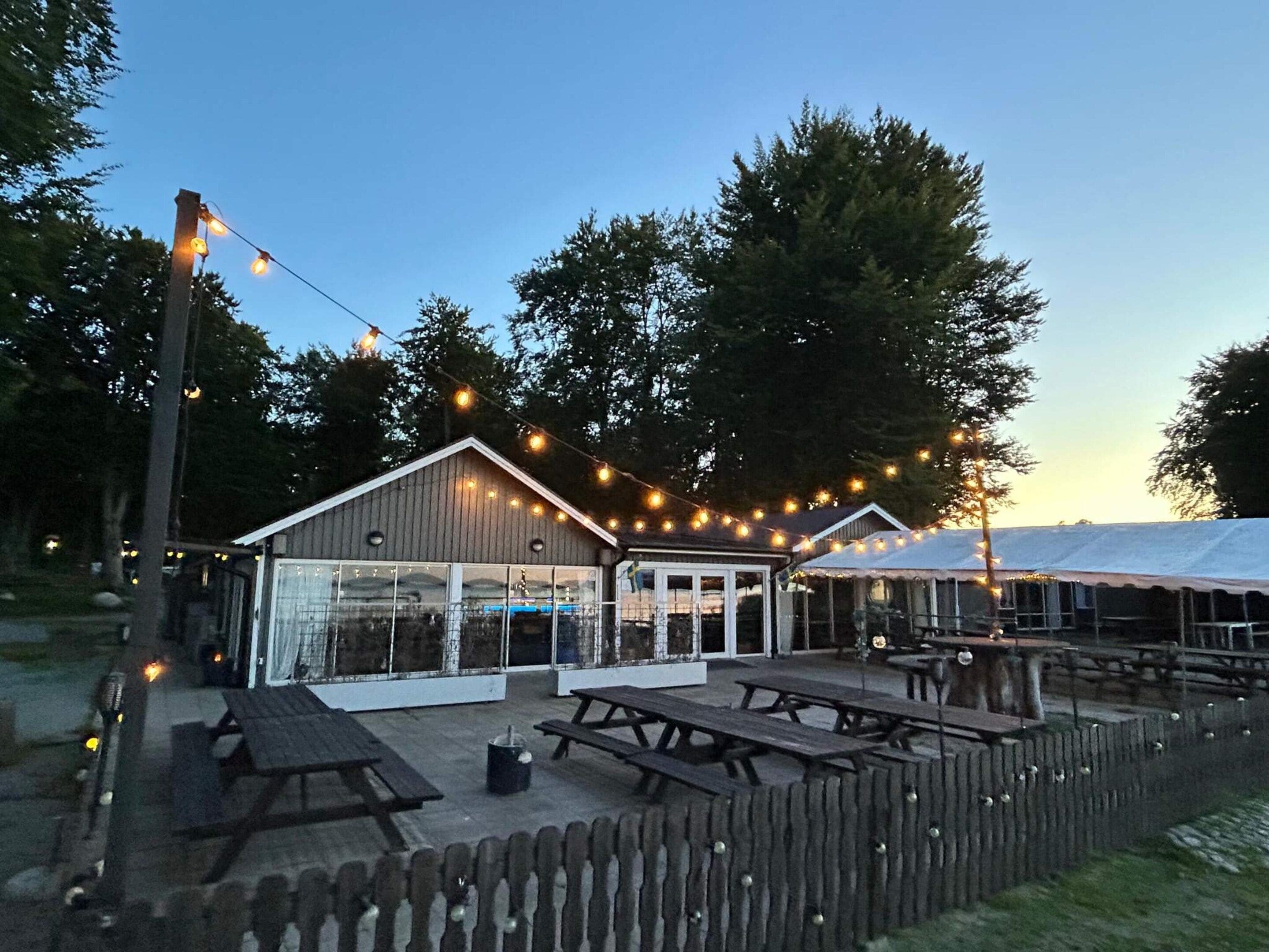 A wooden fence, picnic tables, and string lights.