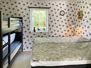 A bedroom with a bunk bed, a single bed, floral wallpaper, a window with plants, a clock, and a framed picture on the wall. - 4 Star Holiday Home in Solvesborg (Sölvesborg)