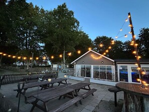 An outdoor patio area with wooden picnic tables and string lights. - 4 Star Holiday Home in Solvesborg (Sölvesborg)