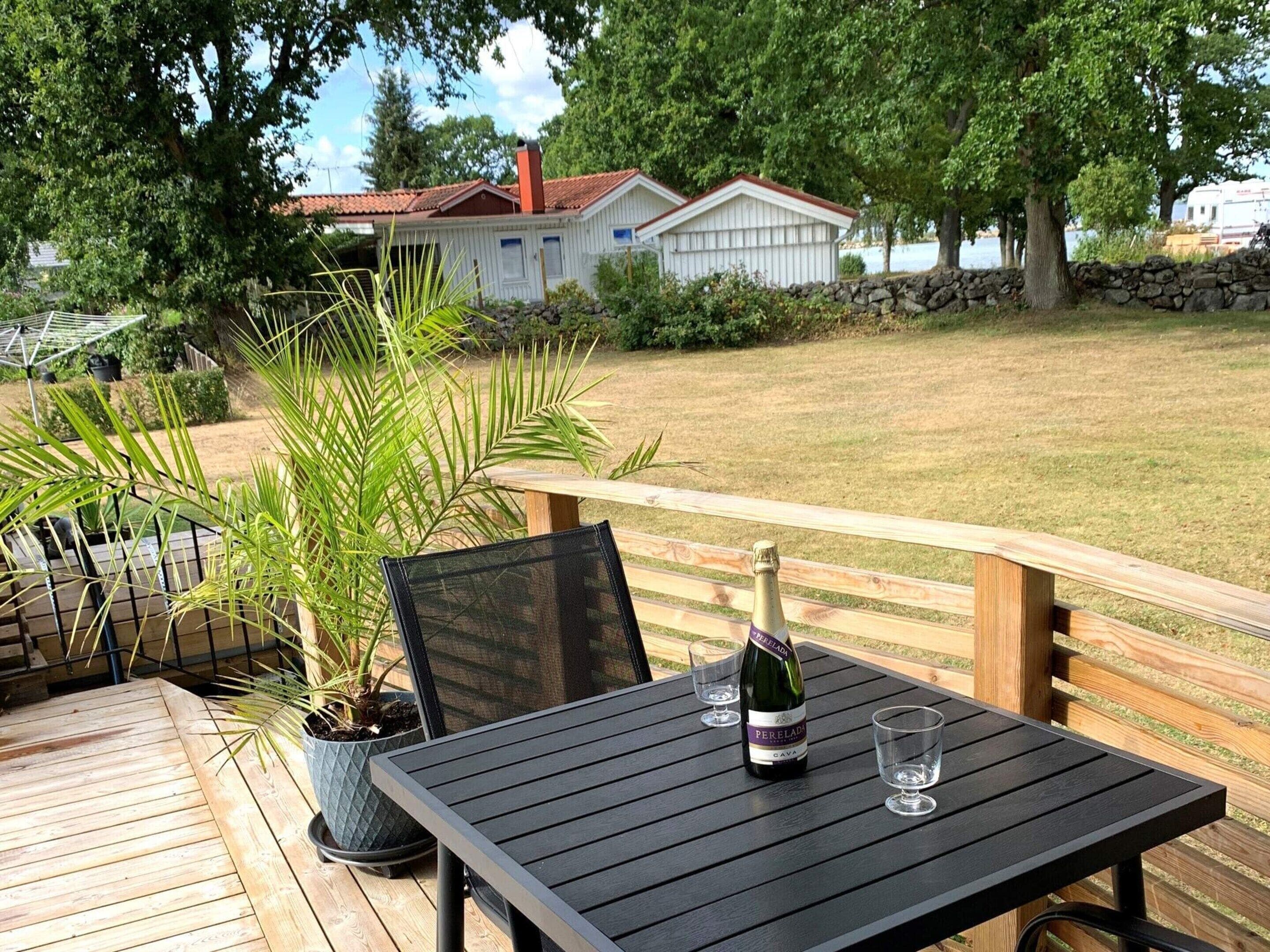 Eine Holzterrasse mit Tisch und Stühlen, einer Weinflasche und zwei Gläsern.