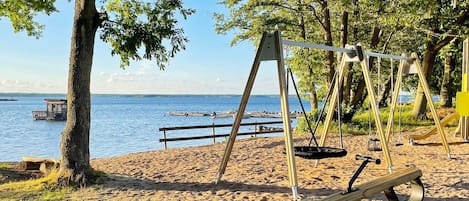 A beach with a swing set, a wooden bench, and a small dock in the water.