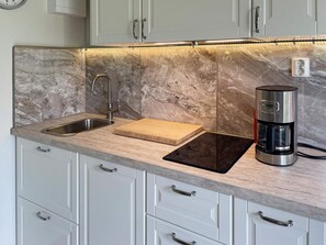 A kitchen with a marble backsplash, stainless steel sink, wooden cutting board, and a coffee maker.