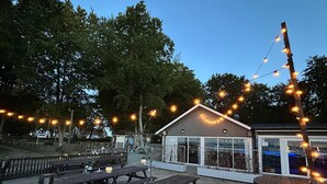 An outdoor patio area with wooden picnic tables and string lights. - 4 Star Holiday Home in Solvesborg (Sölvesborg)