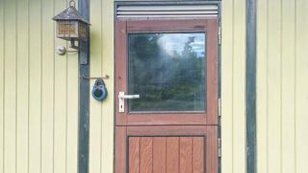 A wooden door with a window, a doorbell, and a wall-mounted light fixture. - 7 Person Holiday Home in Karrebaeksminde (Karrebæksminde)