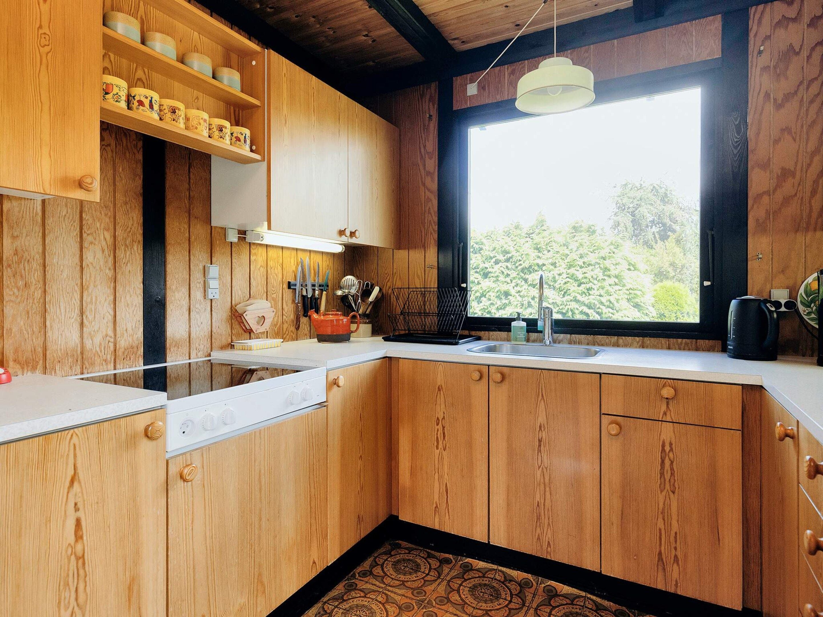 A kitchen with wooden cabinets, a white countertop, a window with a view of greenery, and a hanging light fixture.