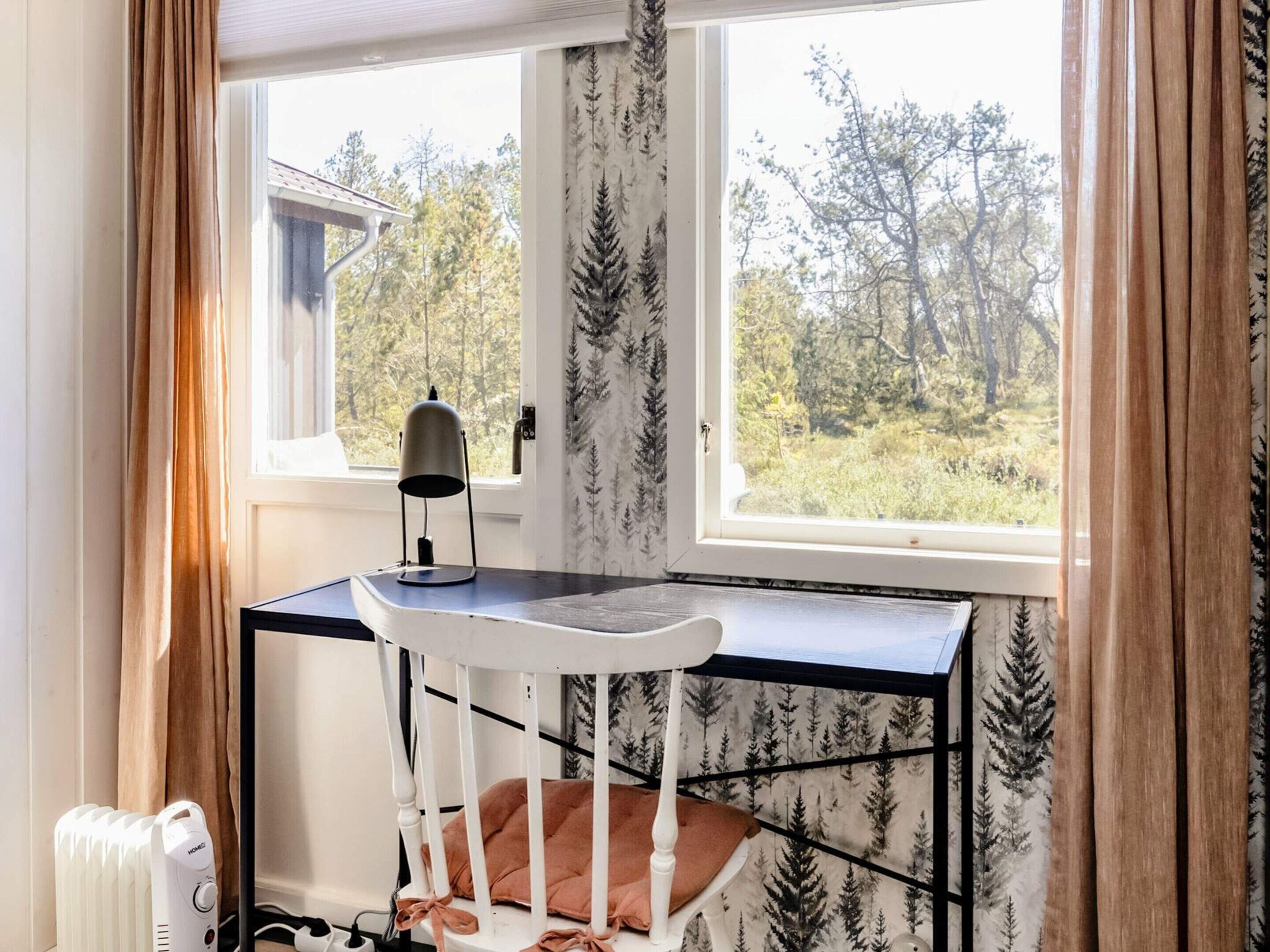 A room with a desk and chair by a window, a radiator, and a view of trees.