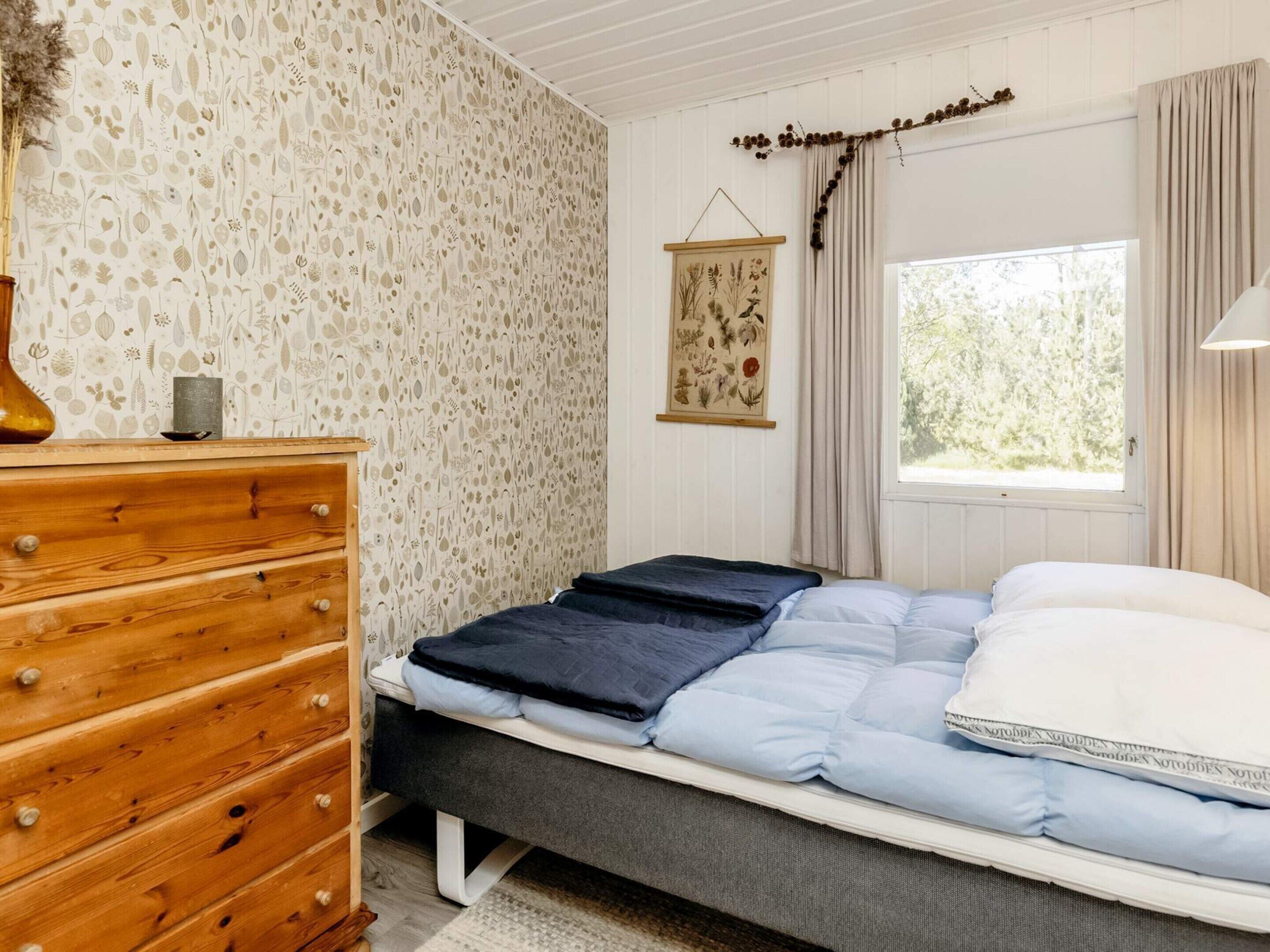 A bedroom with a bed, wooden dresser, and a window with curtains.