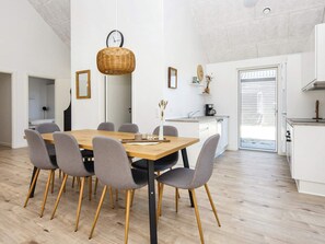 Una cocina moderna con armarios blancos, un comedor con mesa de madera y sillas grises, y una cesta de mimbre colgante.