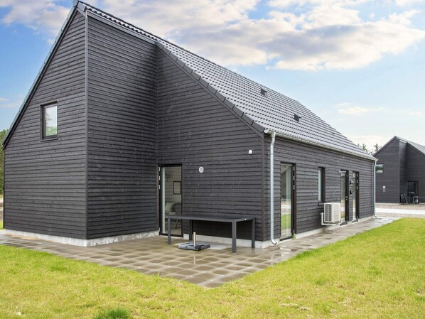 A modern building with a sloped roof, large windows, and a patio area with a table and chairs. - 5 Star Holiday Home in Romo (Rømø)