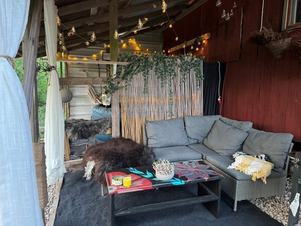 A cozy outdoor seating area with a sofa and a table, surrounded by a wooden fence and string lights.