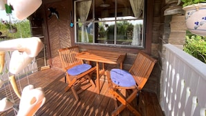 A wooden deck with a table and chairs, a large window with curtains, and hanging planters. - 3 Person Holiday Home in Munkforss (Munkfors)