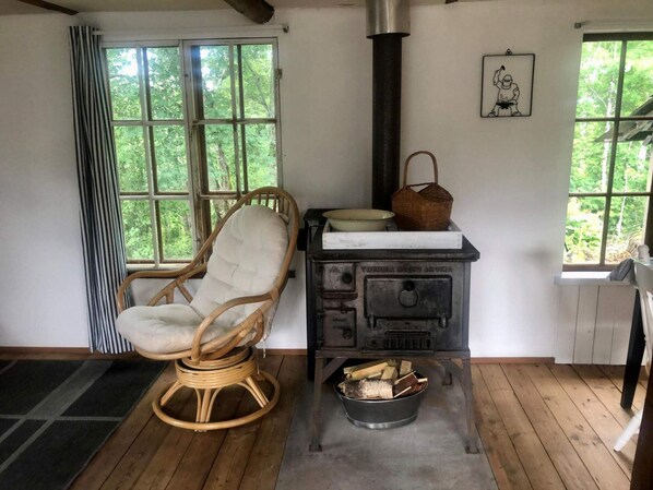 A cozy room with a wicker chair, a stove, and a window with a view of greenery. - 3 Person Holiday Home in Munkforss (Munkfors)