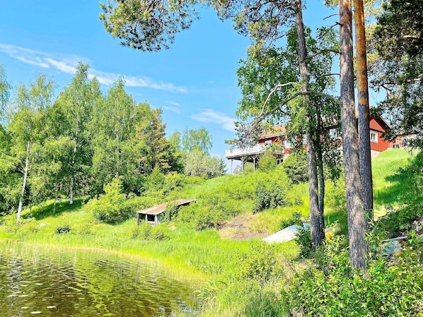 A serene lakeside setting with a small wooden structure, surrounded by lush greenery and tall trees. - 4 Star Holiday Home in Norrtalje (Norrtälje)