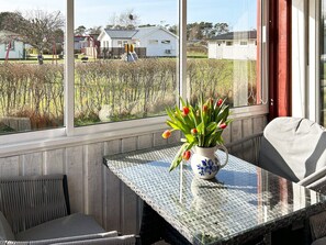 A conservatory with a glass table, a chair, and a vase of tulips. - 6 Person Holiday Home in Laholm (Skummesloevsstrand)