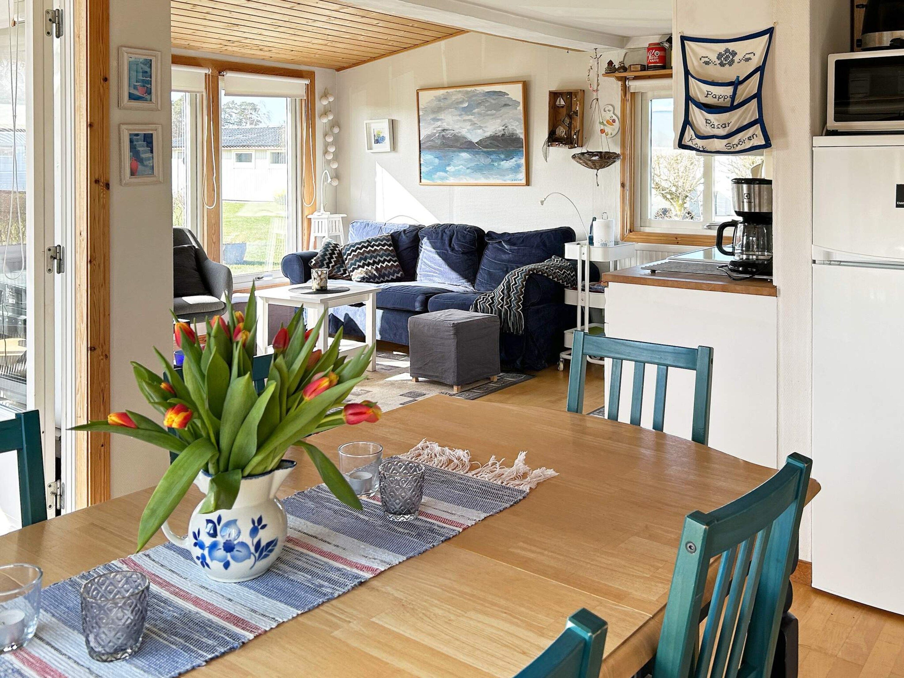 A cozy living area with a sofa, a dining table with chairs, a kitchen area with a refrigerator, and a window with a view of the outdoors.