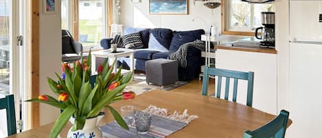 A cozy living area with a sofa, a dining table with chairs, a kitchen area with a refrigerator, and a window with a view of the outdoors.