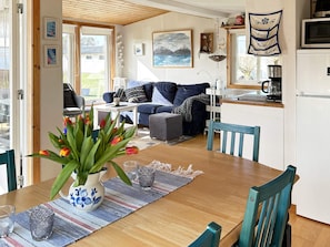 A cozy living area with a sofa, a dining table with chairs, a kitchen area with a refrigerator, and a window with a view of the outdoors. - 6 Person Holiday Home in Laholm (Skummesloevsstrand)