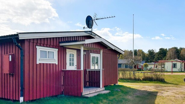 A red wooden cabin with a satellite dish, a door, and a small porch. - 6 Person Holiday Home in Laholm (Skummesloevsstrand)