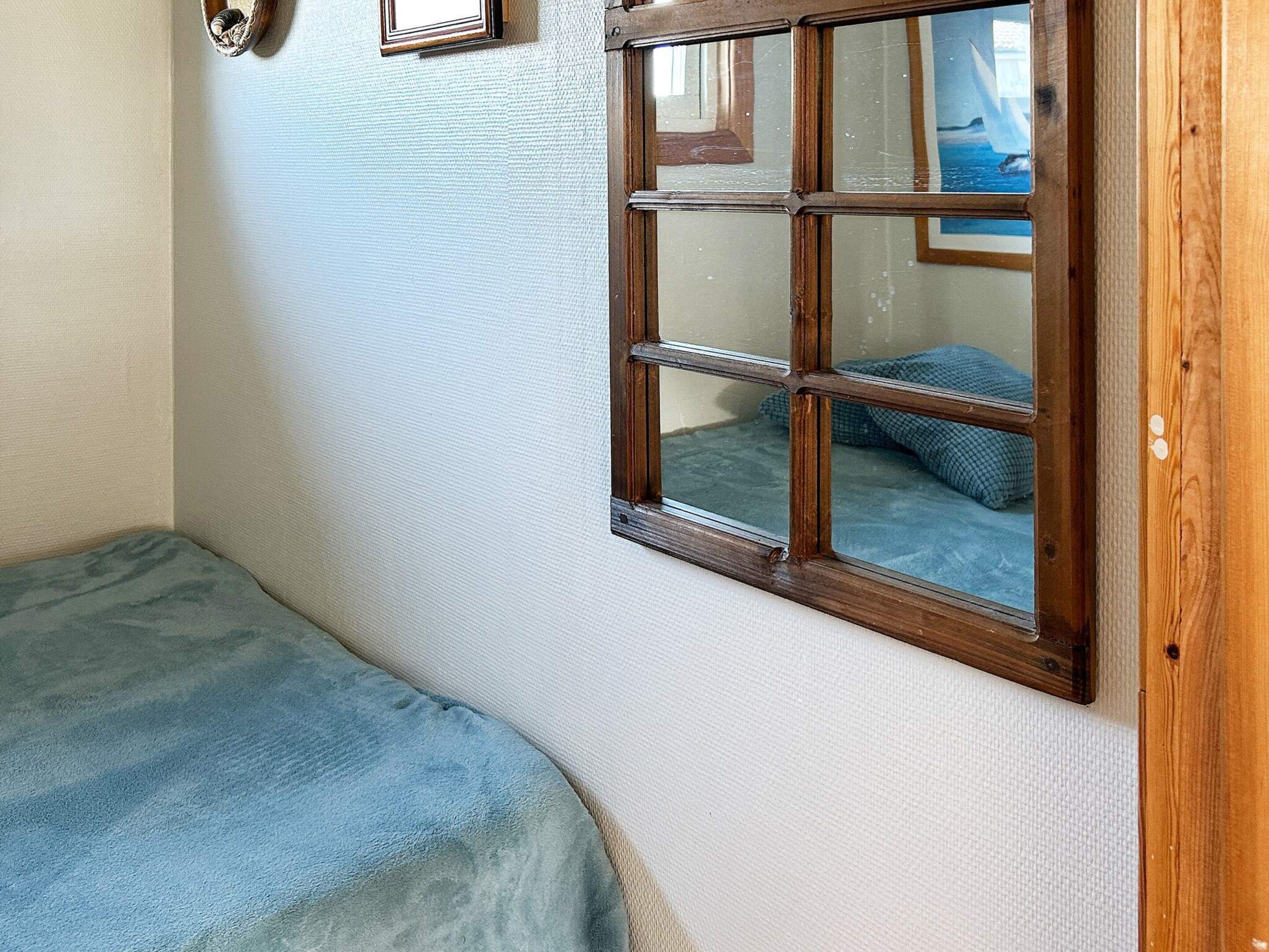 A room with a single bed, a window with a view of the sea, and a wall-mounted picture frame.