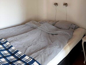A bed with a striped bedspread and pillows, a bedside table, and a wall-mounted light fixture. - 6 Person Holiday Home in Laholm (Skummesloevsstrand)