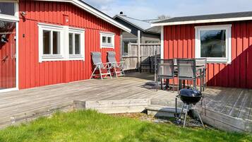 A red building with a wooden deck, two windows, and a barbecue grill.