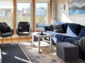 Un salón con un sofá azul, dos sillones, una mesa de centro y vistas a una zona residencial a través de amplios ventanales.