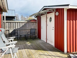 A wooden deck with outdoor seating and a red building with a door and window. - 6 Person Holiday Home in Laholm (Skummesloevsstrand)