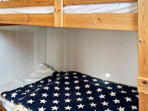 Een stapelbed met een witte matras en een marineblauwe deken met witte sterren.