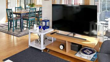 A living room with a flat-screen TV, a coffee table, a sofa, and a dining area with chairs and a table.
