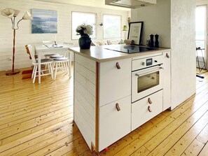 Een kleine keuken met een centraal eiland, houten vloeren en een eethoek met witte stoelen.